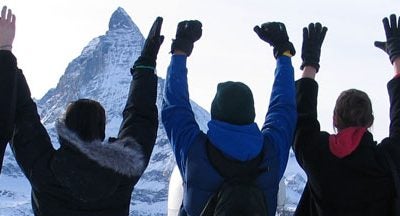 Group of people with their backs to the camera, raising their hands, with a mountain in the background