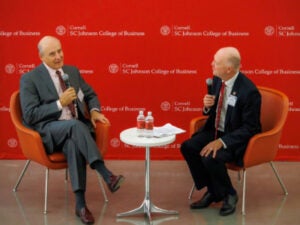 Eduardo Padilla and Dean Andrew Karolyi talking on red seats on stage, with a red Cornell banner in the background