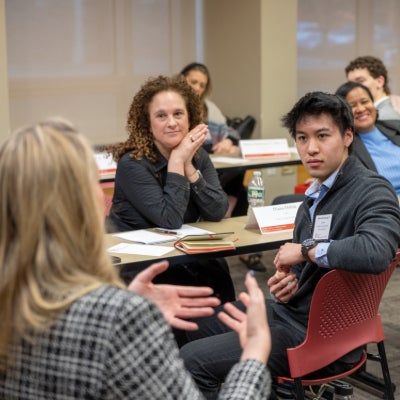 Alex Cheung seated at a table speaking to two females dressed in professional attire.