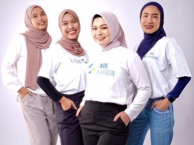 Four women standing side by side, dressed in white T-shirts with Nol Karbon logos against a clean light background.