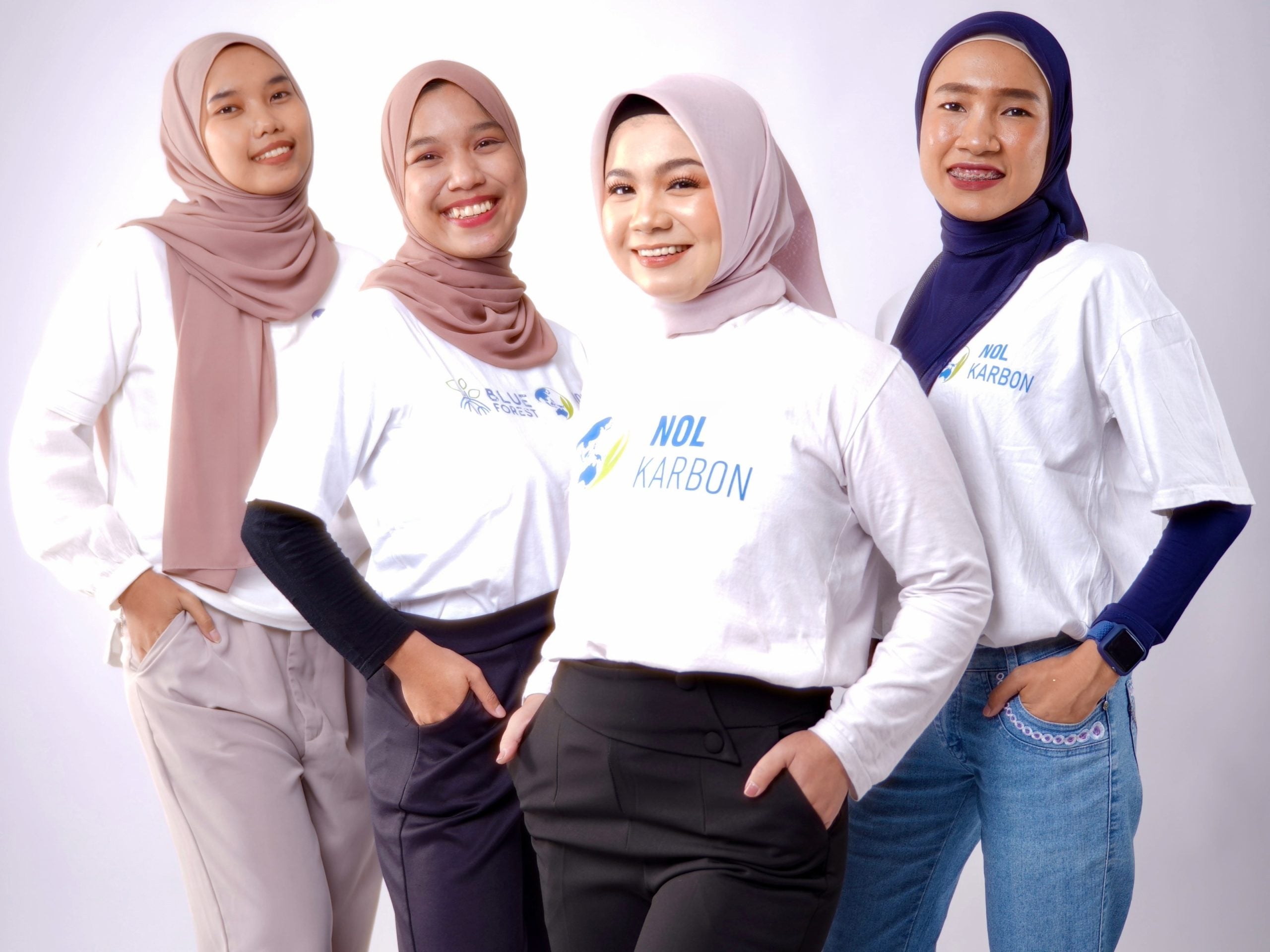 Four women standing side by side, dressed in white T-shirts with Nol Karbon logos against a clean light background.