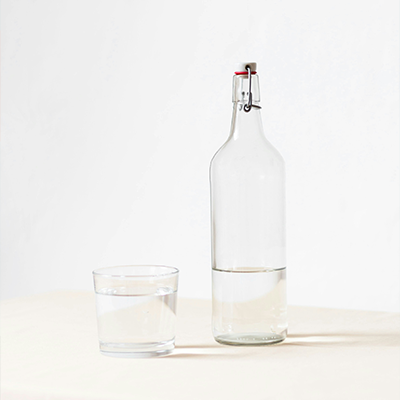 Glass of water next to a bottle.