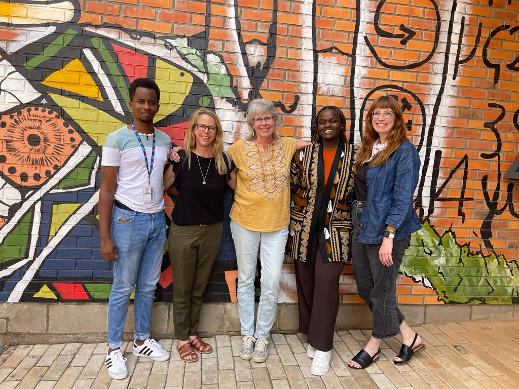 Cornell facilitators and Rwandan stakeholders pose in front of a brightly painted wall art.