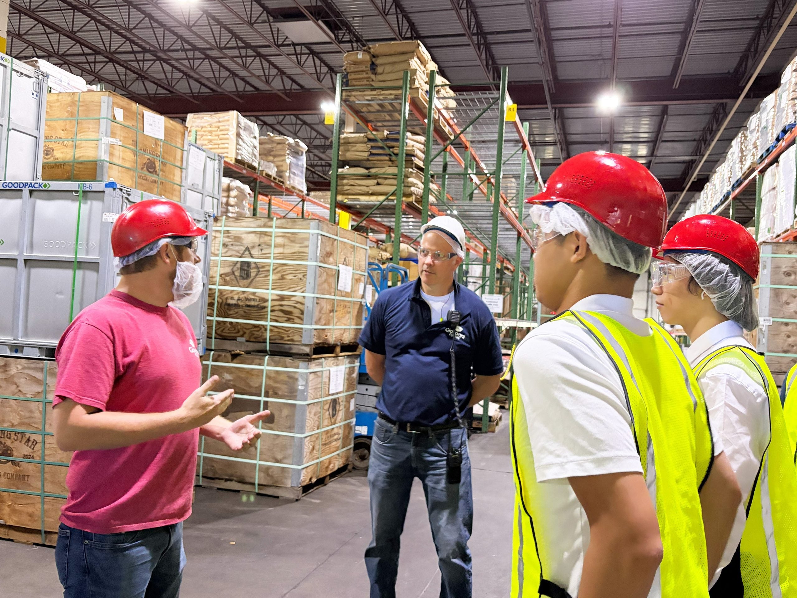 A group of students wearing hard hats speaking with a representative from Giovanni Foods in a warehouse.