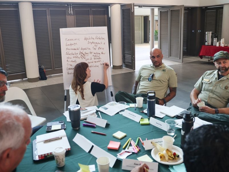 A woman writes on a large easel pad while people sit around a round table.