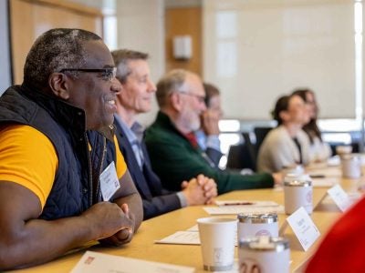 A smiling man sits in the foreground of a roundtable discussion session.