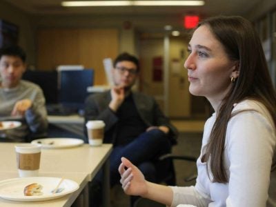Grace Van Hollebeke ’19 (CALS) speaks at a table with two people visible in the background.