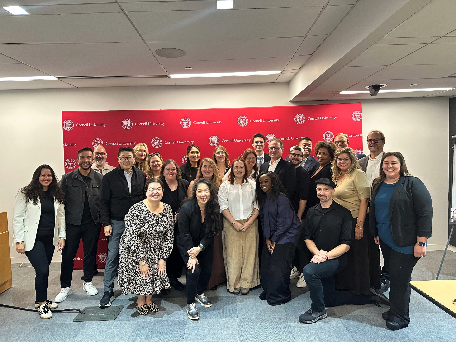 A group of people gathered in front of a red Cornell backdrop for a group photo.