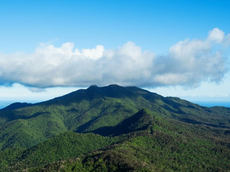 Green mountains with a blue sky overhead with low-level clouds.
