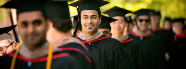 A graduating student smiles among a group of peers wearing robes