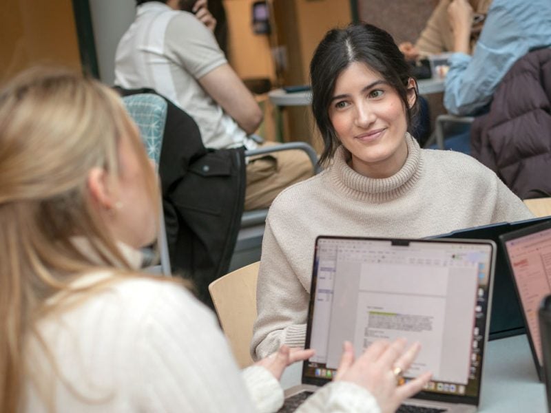 Two women work together on their laptops