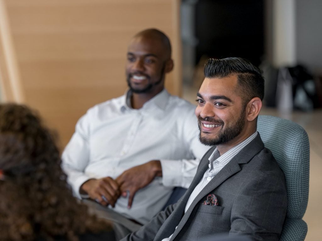 A young man in business casual attire smiles towards a classmate speaking to him as part of a social event of the Cornell MBA experience